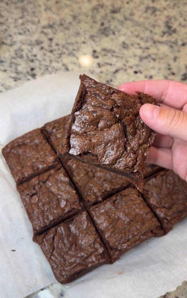 Square cut soft and fudgy brownies. One is being held up showing the brownie's soft texture .