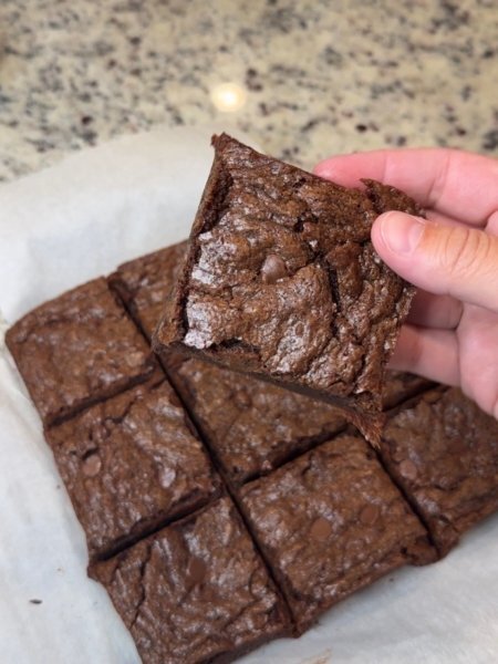 Square cut soft and fudgy brownies. One is being held up showing the brownie's soft texture .