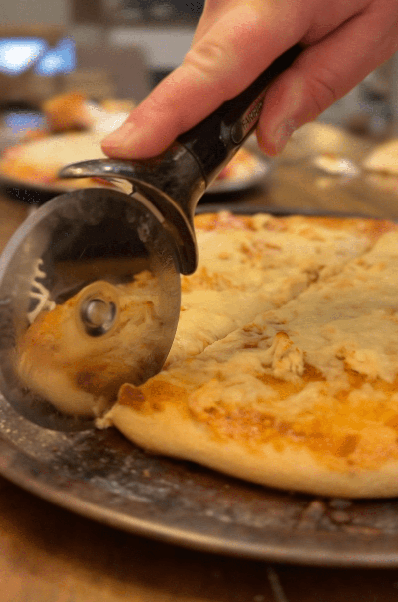 Pizza with pizza cutter and hand