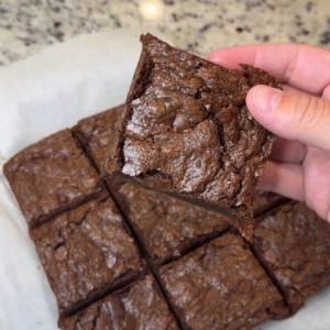 Square cut soft and fudgy brownies. One is being held up showing the brownie's soft texture .